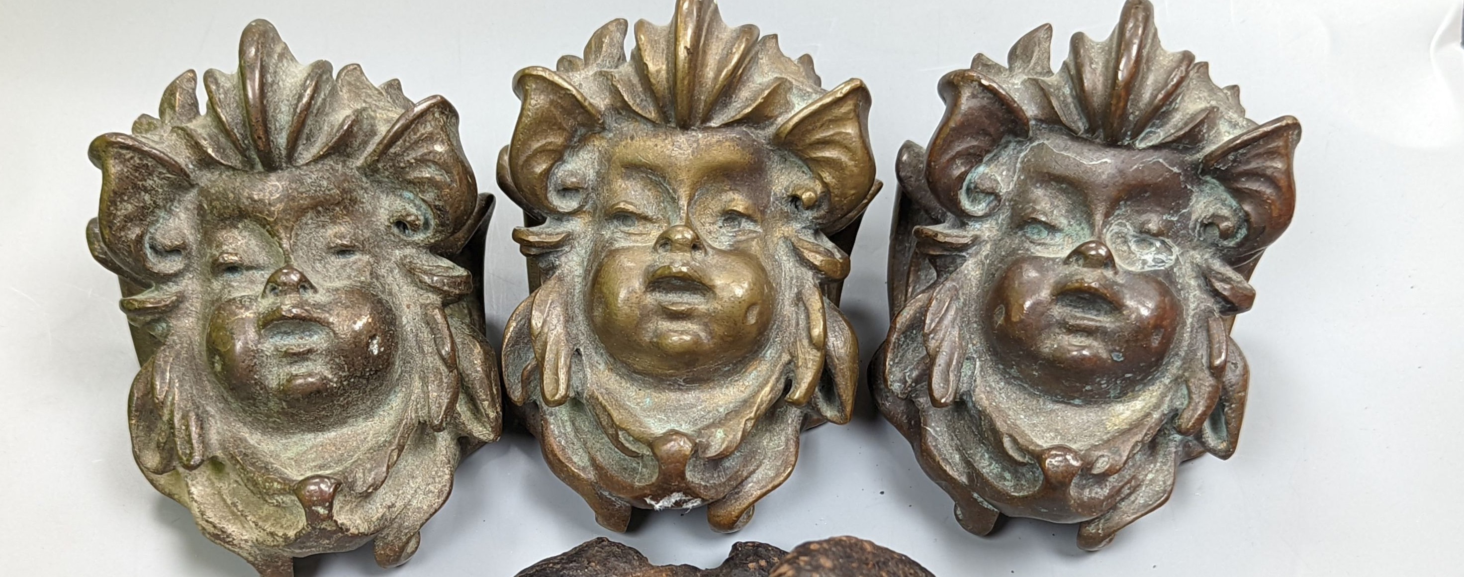 A set of three cast bronze mask-form furniture mounts, 9cm. high